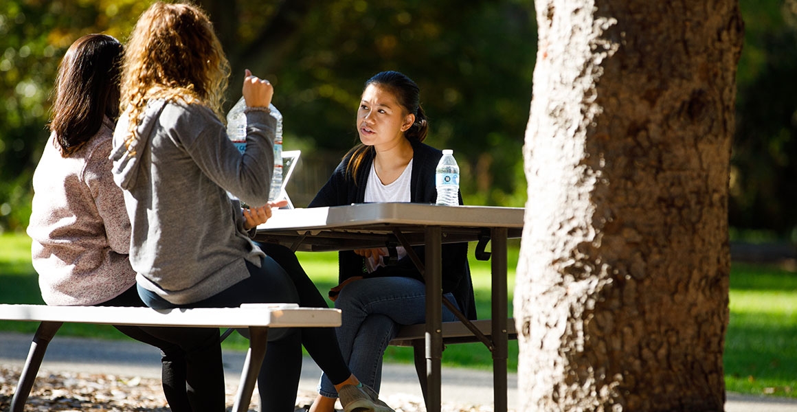 three women at a picnic table having a conversation