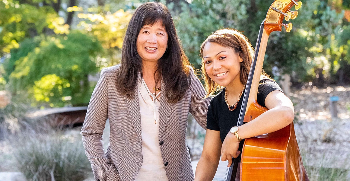 two women smiling, one holds a bass instrument